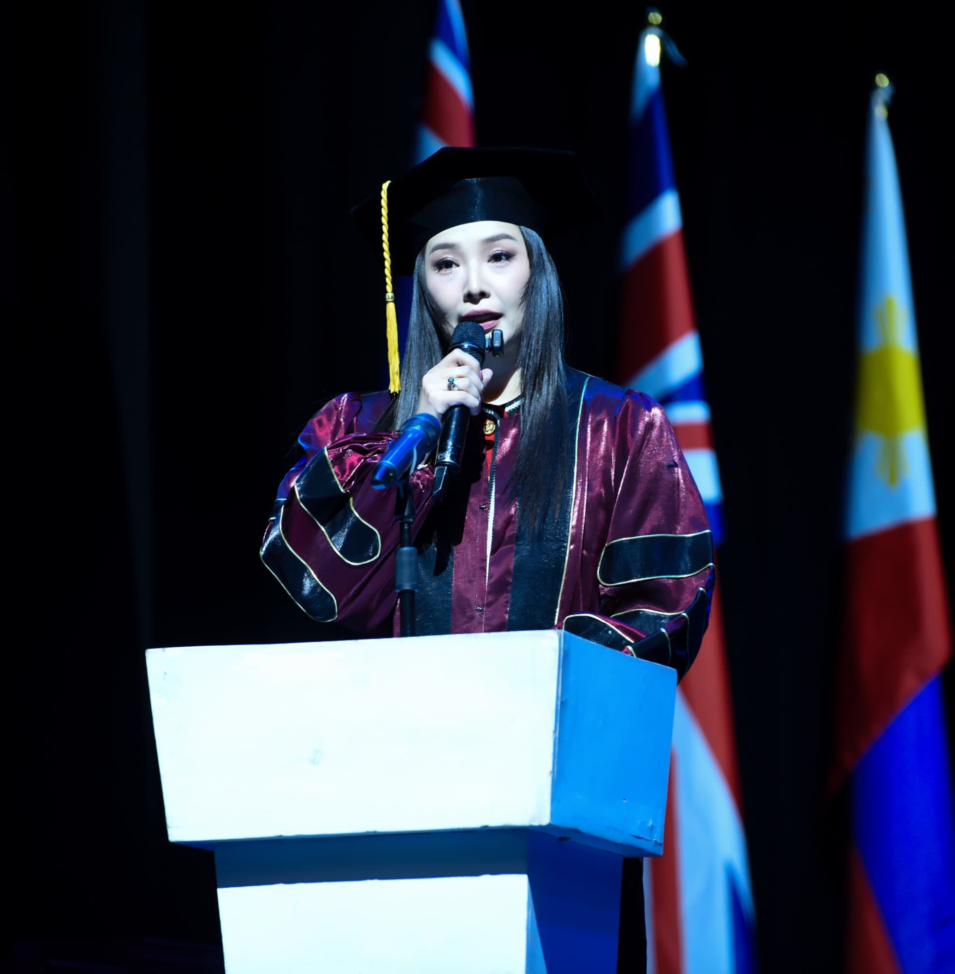 A graduate speaks at the podium before international flags