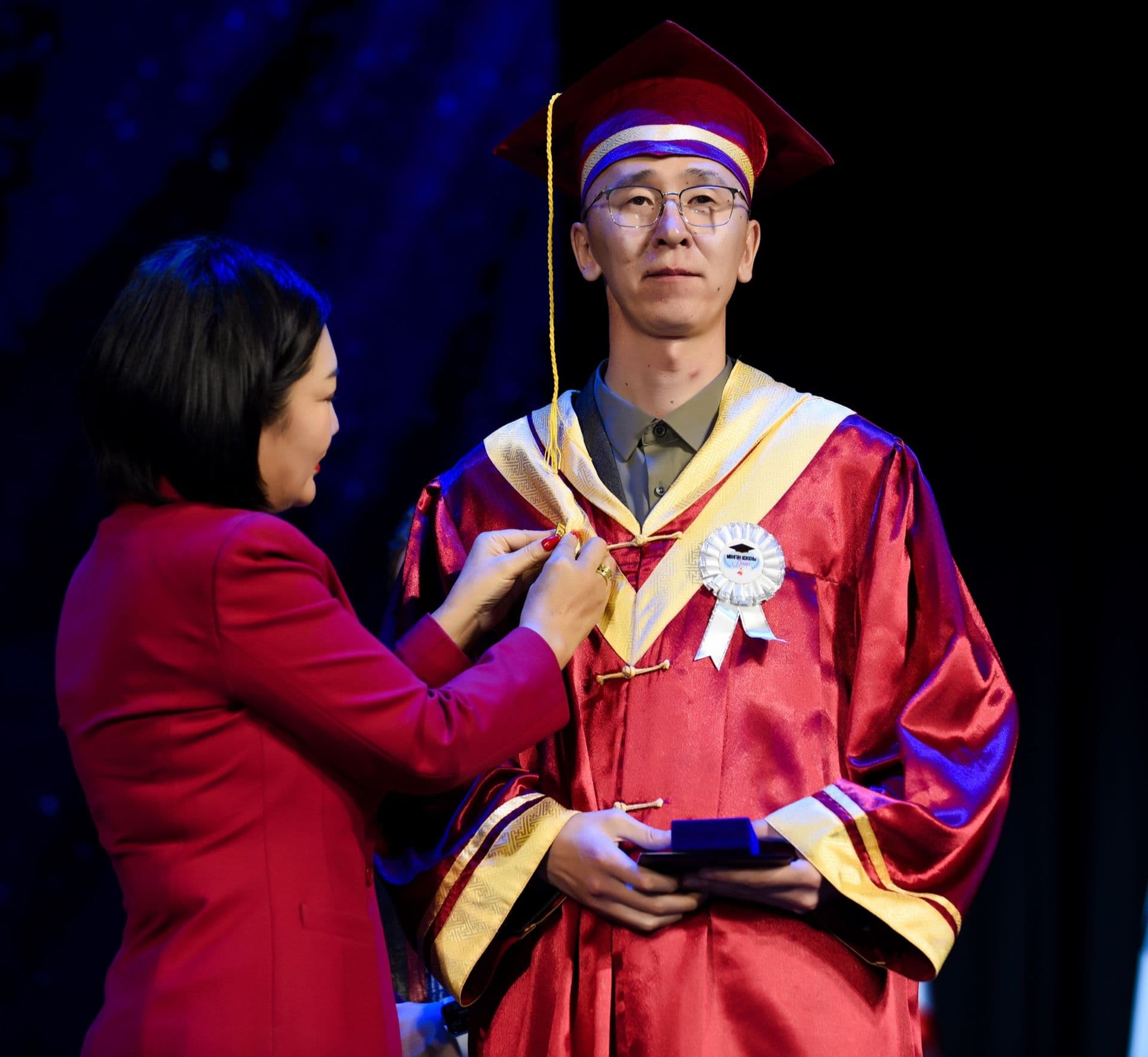 A master’s graduate is hooded on stage